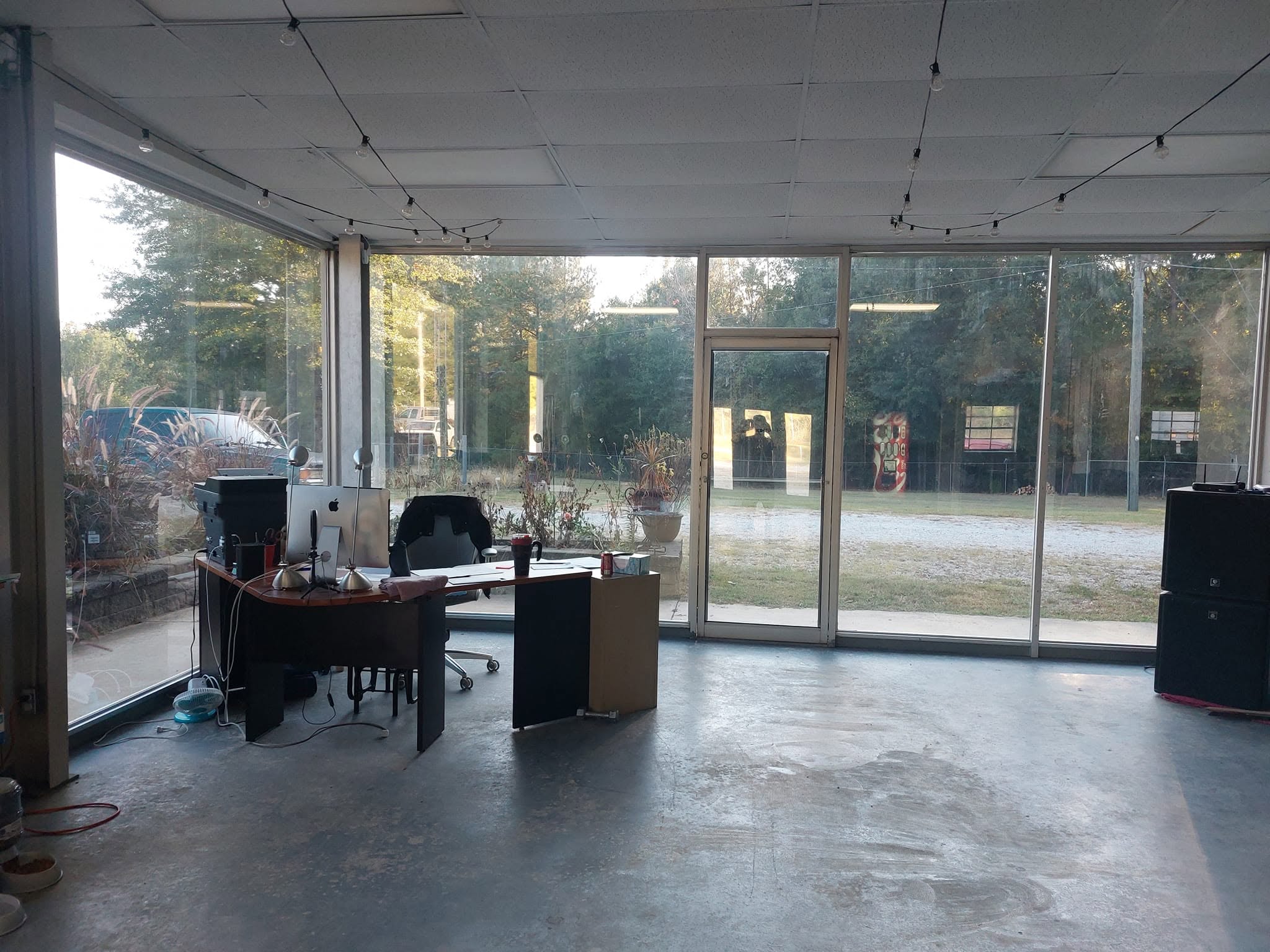 Modern office space with concrete floors, glass walls, and minimal furniture overlooking outdoor landscape