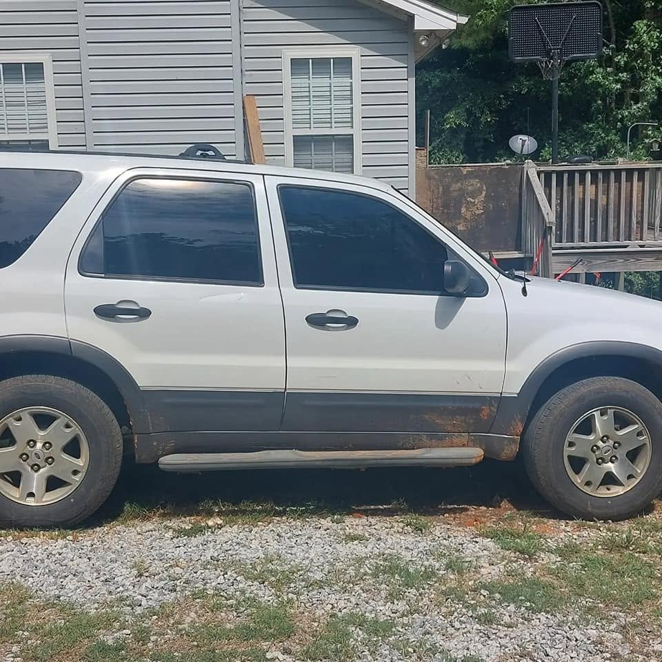 White and dark gray SUV with rust on lower panels parked in gravel driveway near house