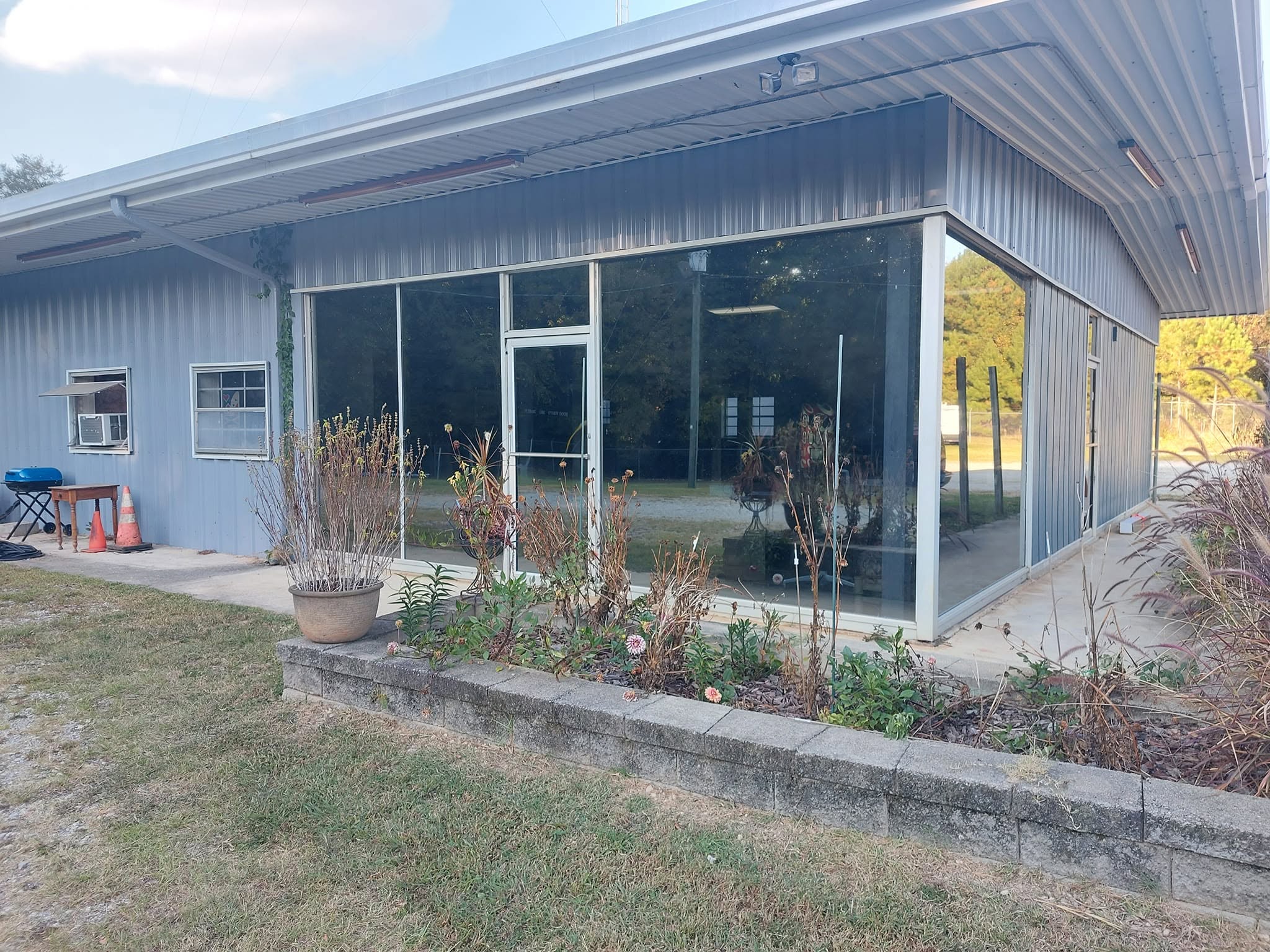 Modern metal-frame building with screened porch, large windows, and concrete patio surrounded by landscaping