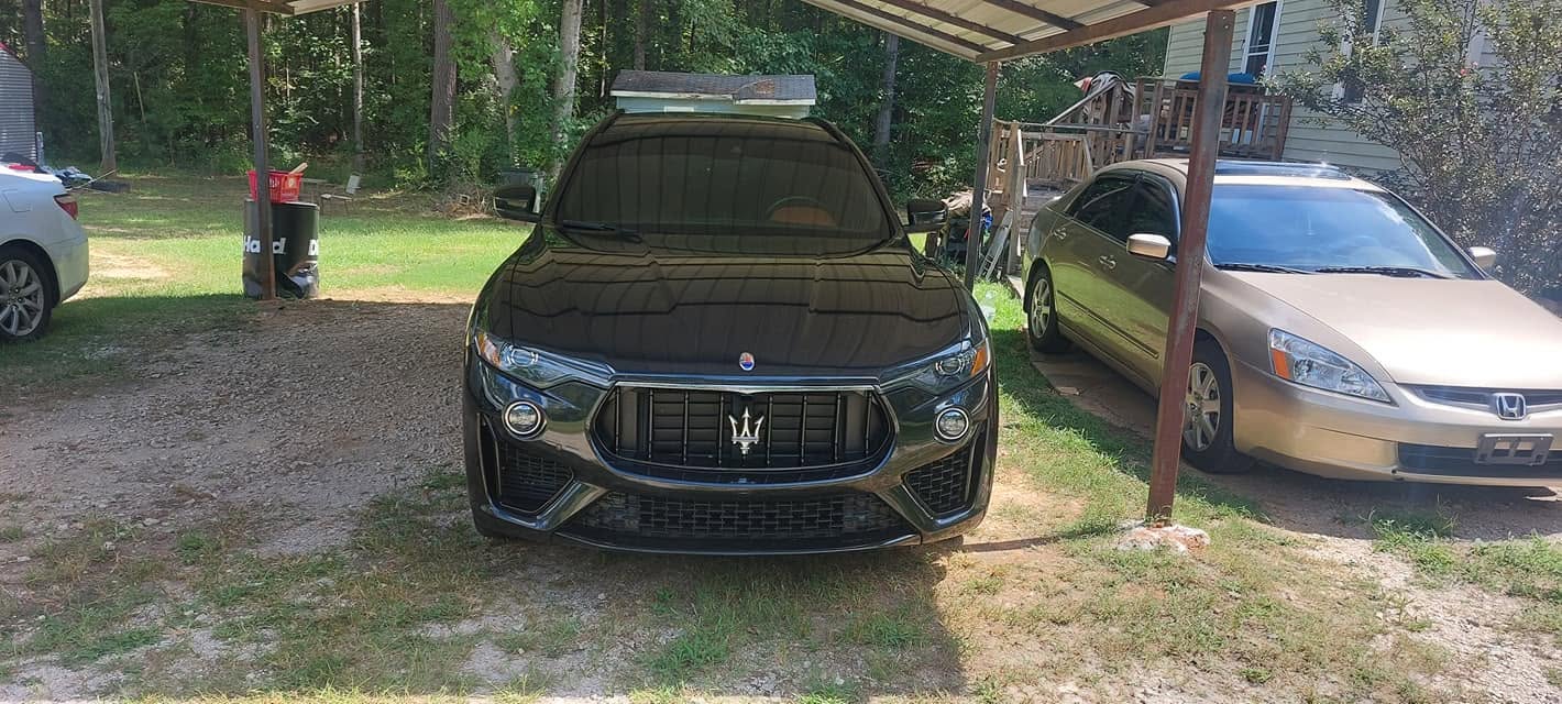 Black Maserati SUV parked in driveway under wooden carport with other vehicles nearby