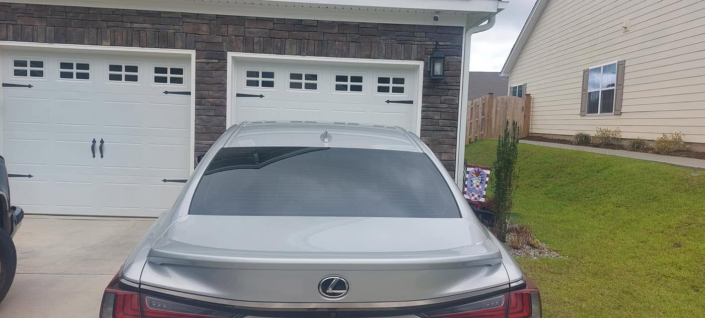 Silver Lexus sedan parked in driveway with white garage doors and brick house