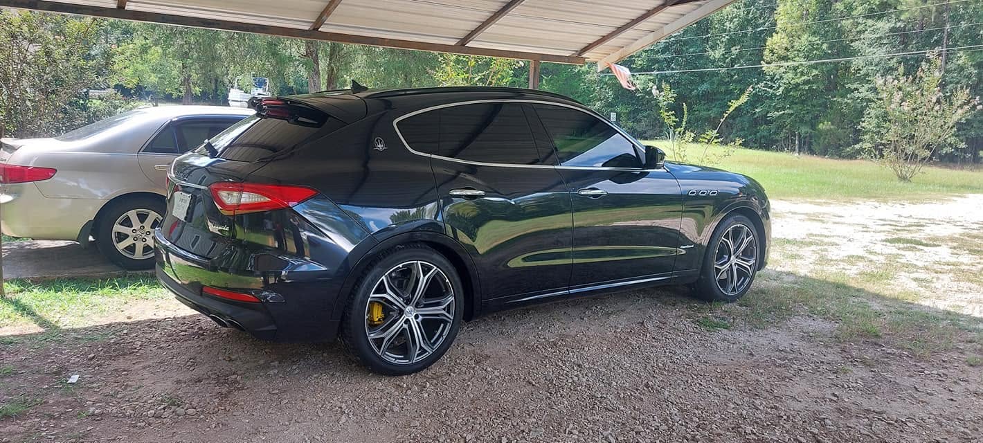 Black Maserati luxury sports car parked under carport with silver sedan in background