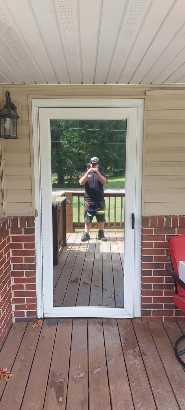 Man in cap and dark shirt standing on wooden deck taking selfie through glass door