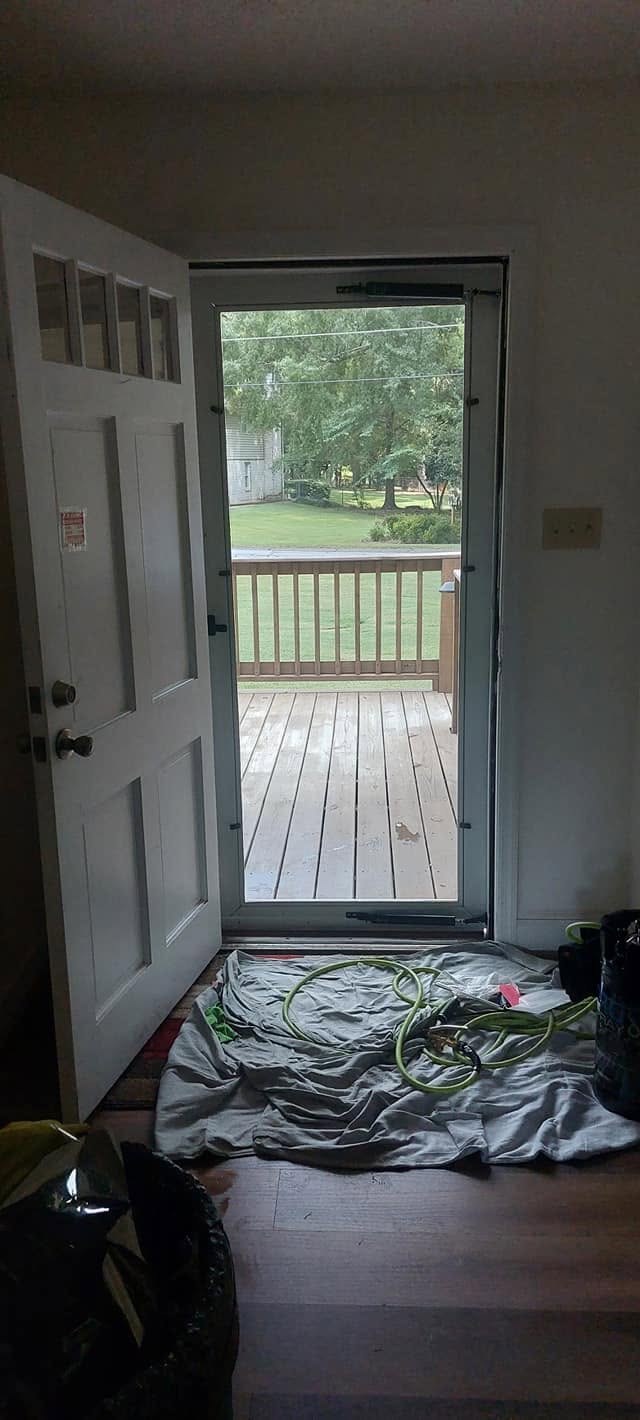Open glass door showing deck with railing, green lawn and trees beyond