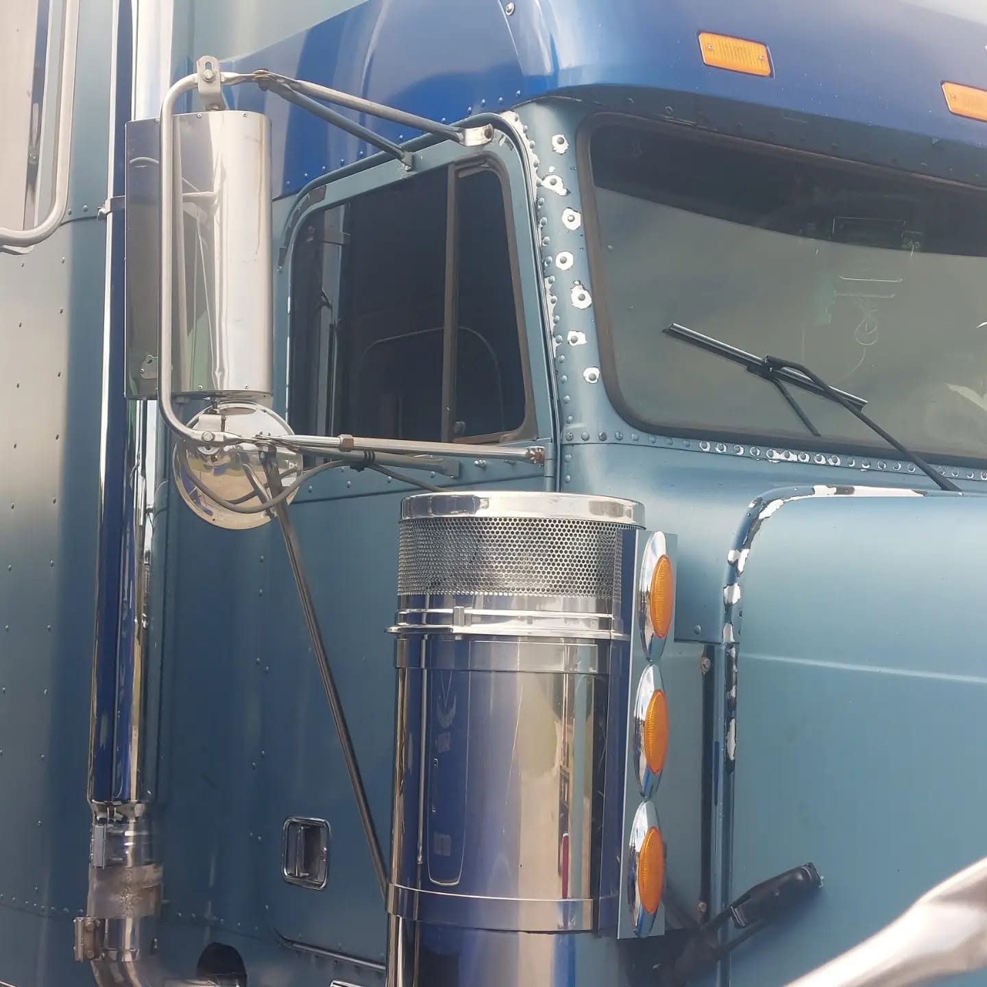 Large blue truck with stainless steel exhaust stack and chrome details mounted on side