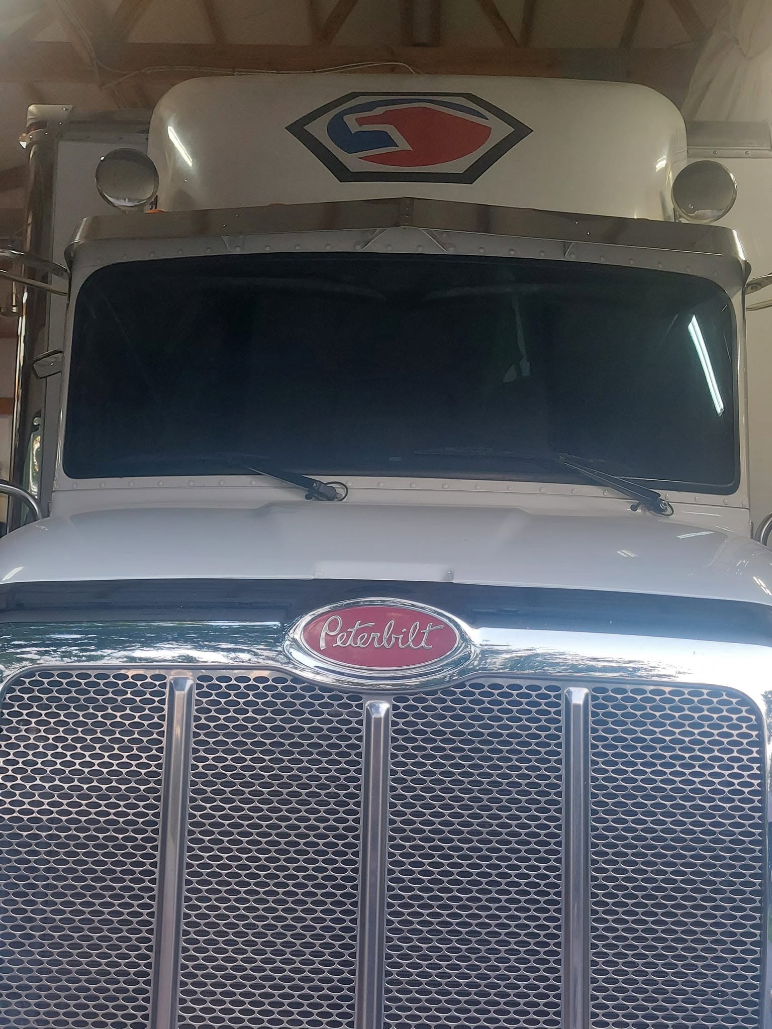 Front view of white Peterbilt semi truck with chrome grille and red oval badge