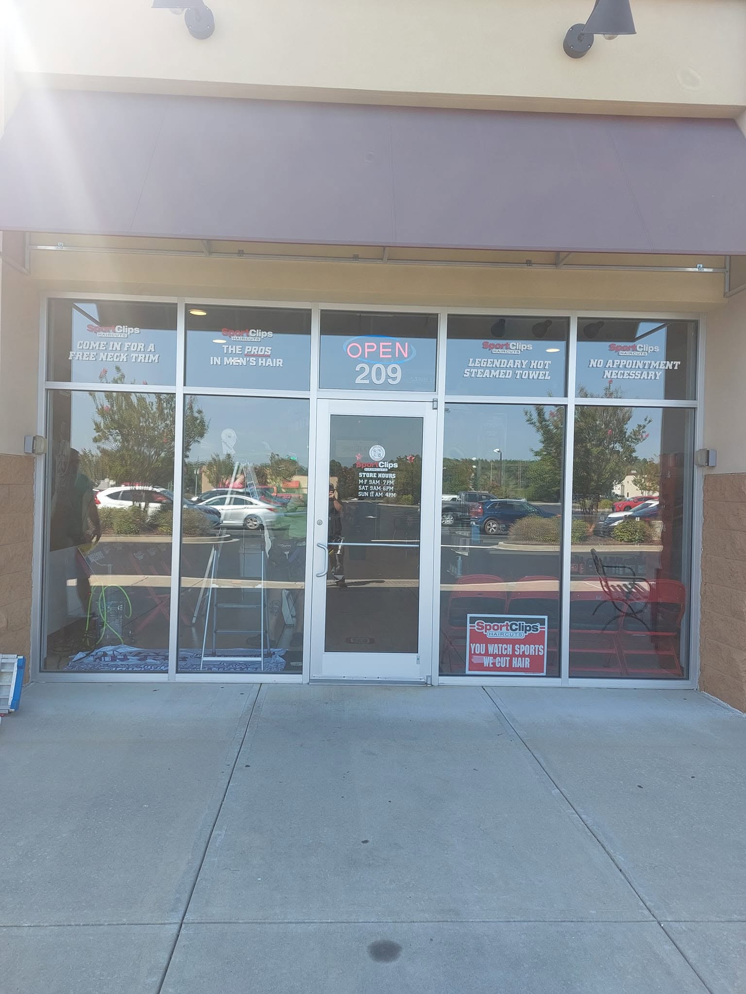 Sport Clips barbershop storefront with glass doors and windows displaying open sign and promotional banners
