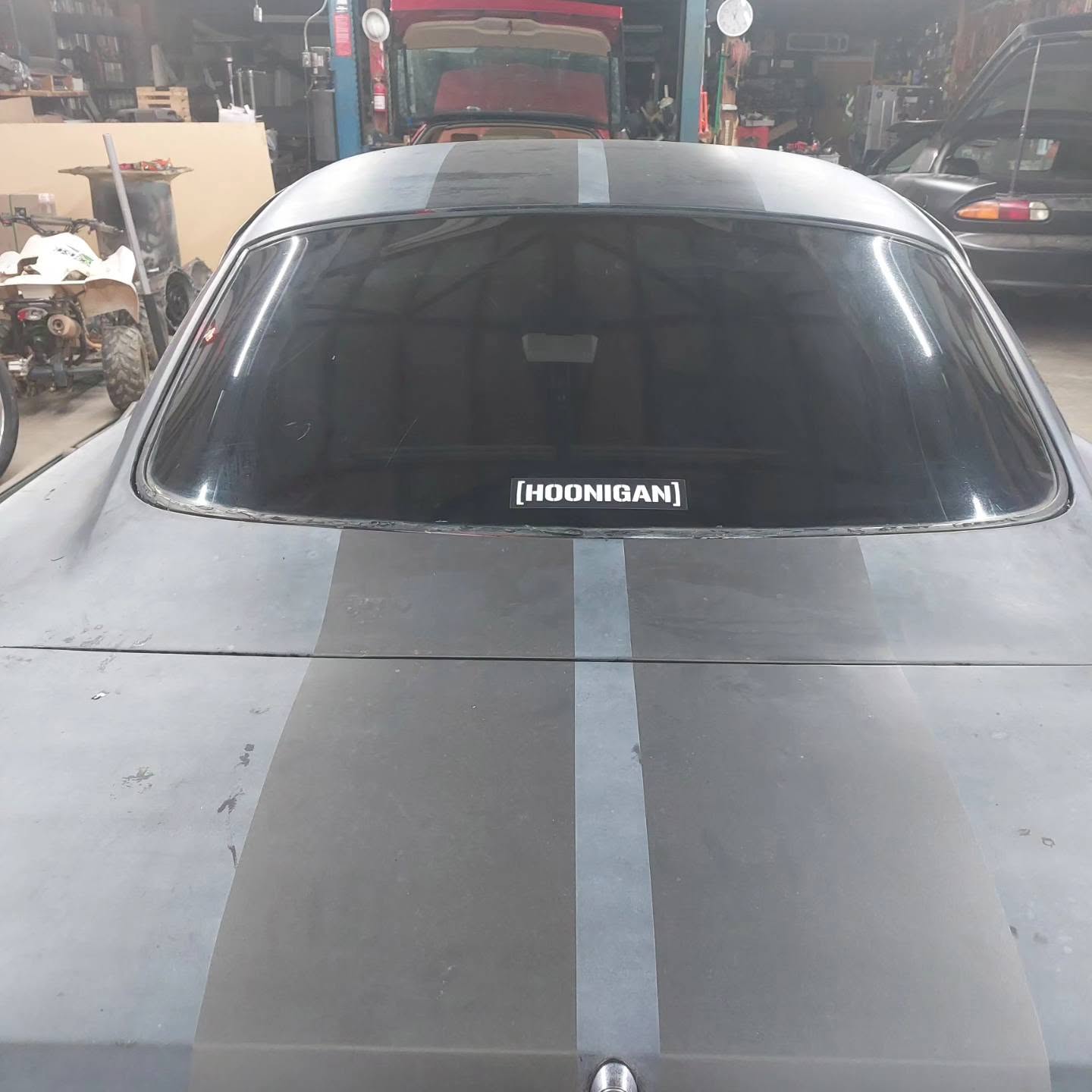 Gray sports car with Hoonigan windshield decal and racing stripes in auto shop