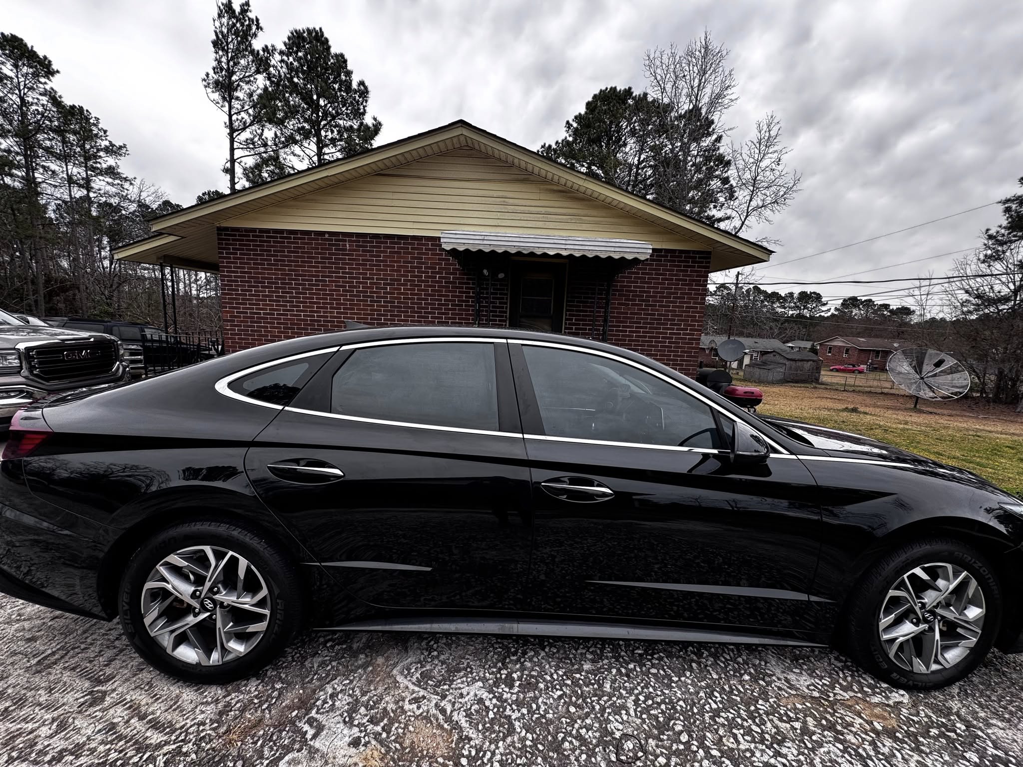 Black sedan parked in front of red brick house with tan roof