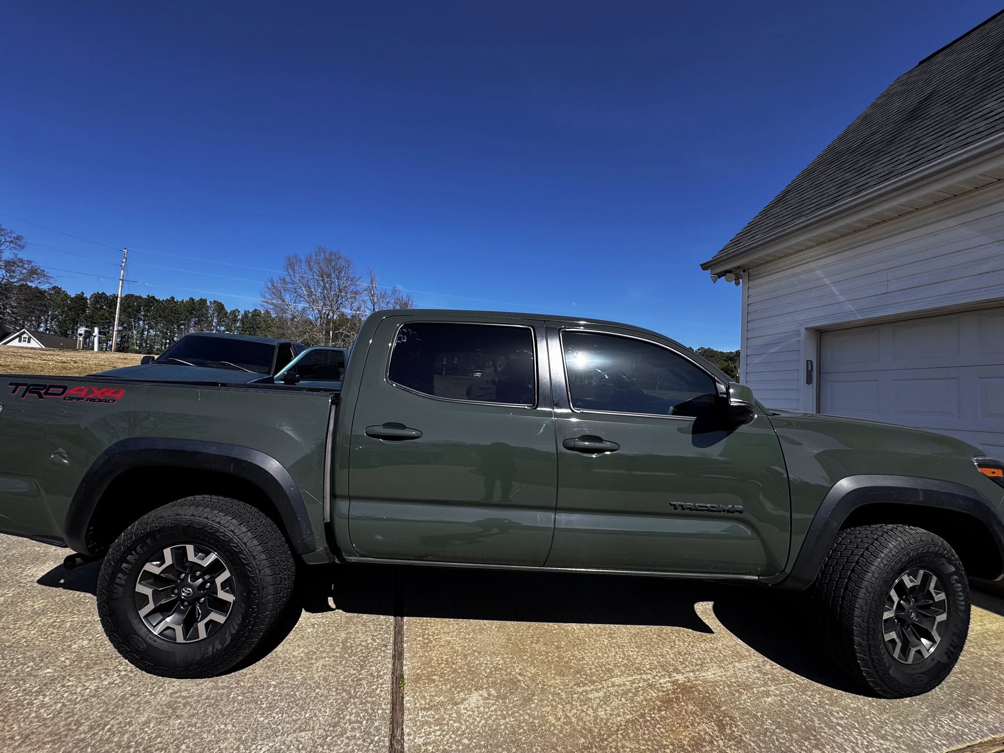 Green Toyota Tacoma pickup truck parked in driveway next to garage