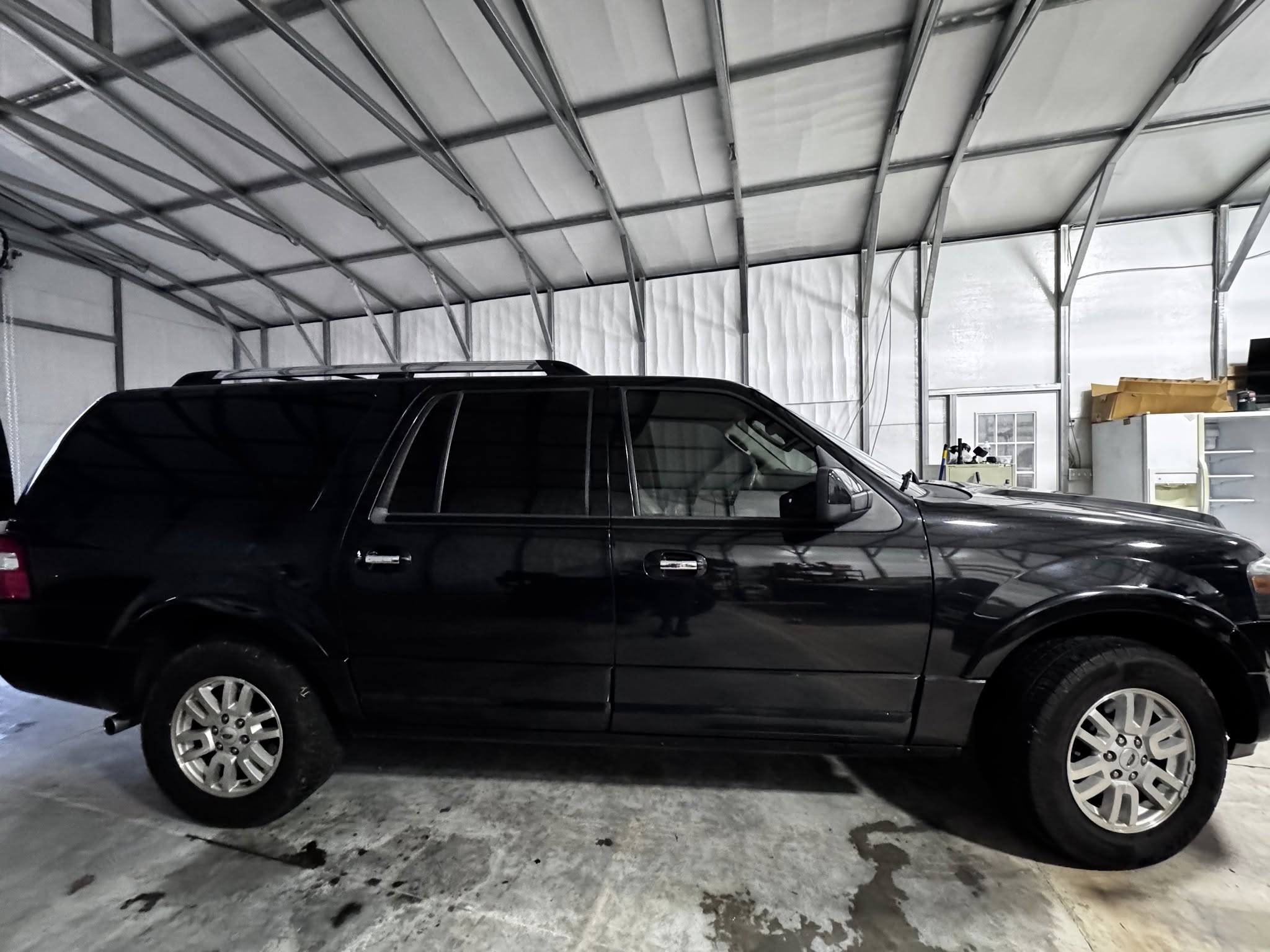 Black SUV parked inside metal-framed garage with translucent white panels